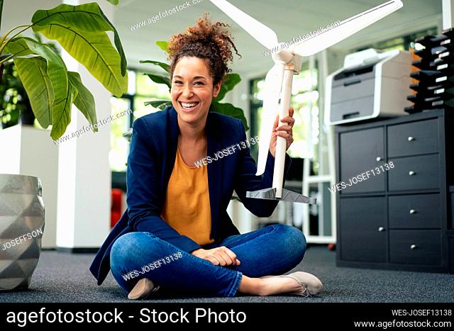 Cheerful businesswoman with wind turbine model sitting in office