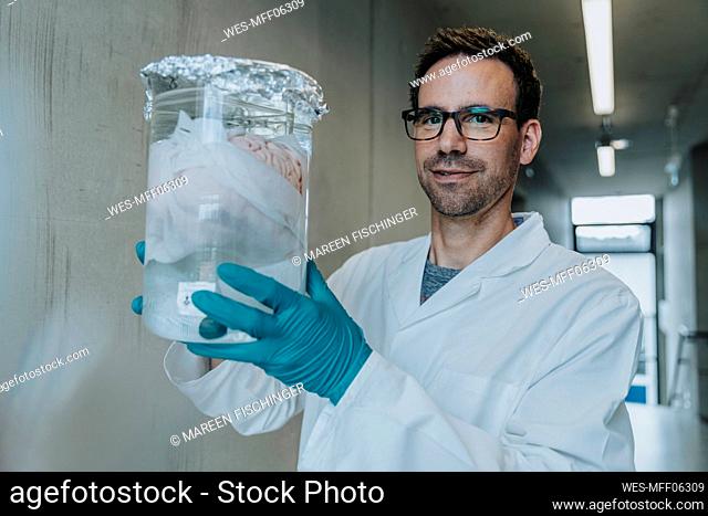 Scientist holding preserved human brain beaker while standing at clinic corridor