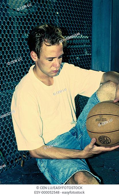 Male teen sitting outdoors with basketball
