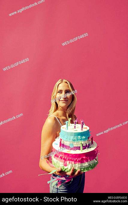 Young woman looking away while carrying birthday cake against wall