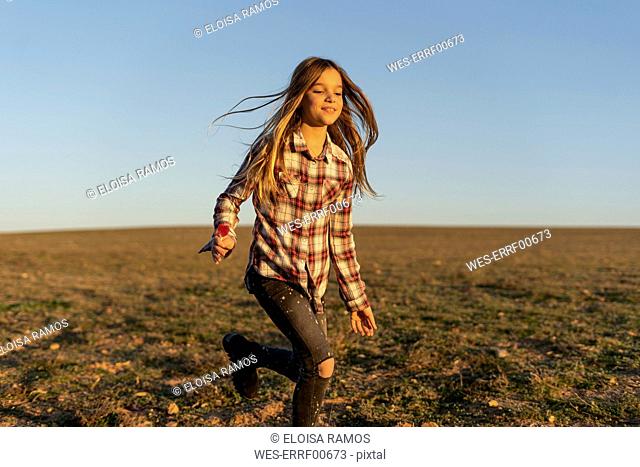 Portrait of smiling girl with lollipop running on pasture by sunset