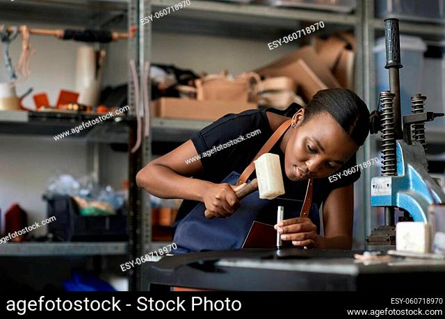 Young African female leather worker using a mallet and punch while working at a bench in her studio
