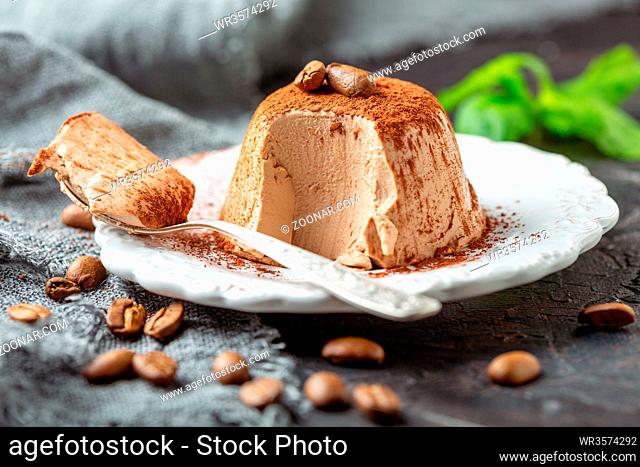 Traditional Italian dessert Panna cotta sprinkled with cocoa powder and decorated with coffee beans on a plate close-up, selective focus