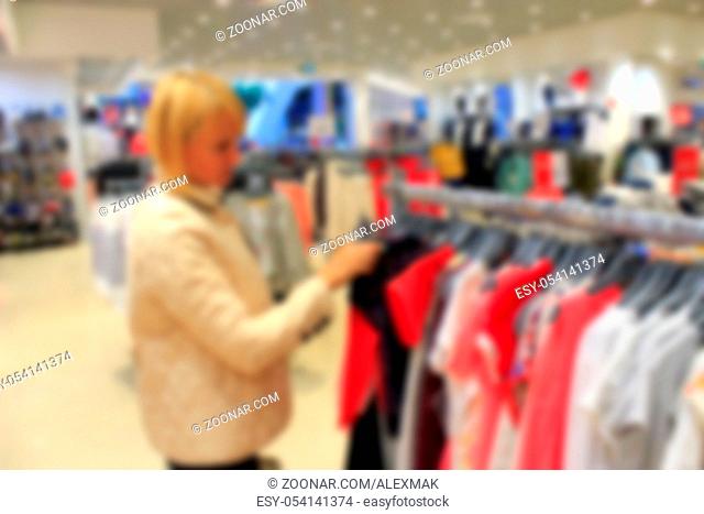 blurred image of the woman chooses clothes among the great assortment in shop of clothing