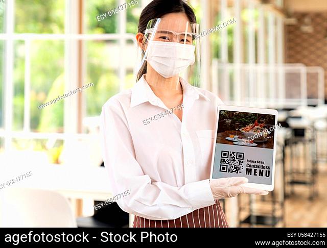Asian waitress with face mask and face shield hold digital tablet with QR code for customer to scan for online contactless menu