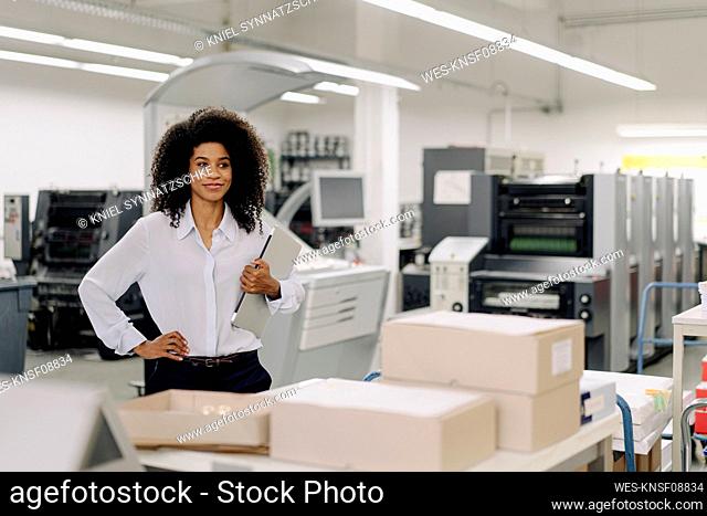 Female professional with hand on hip holding laptop in industry