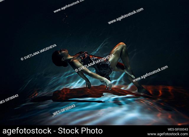 Young woman in silk dress swimming underwater in sea