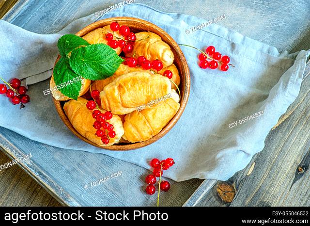 Croissants with currant berries on a wooden tray. The concept of a wholesome breakfast