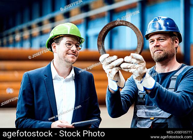 Mature worker checking equipment while standing by male manager in industry