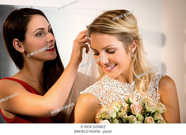 Bridesmaid adjusting veil of bride before wedding