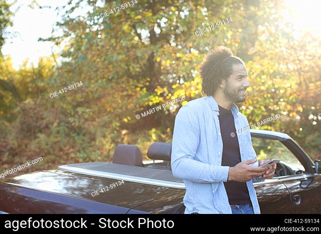 Young man with smart phone at convertible in sunny autumn park
