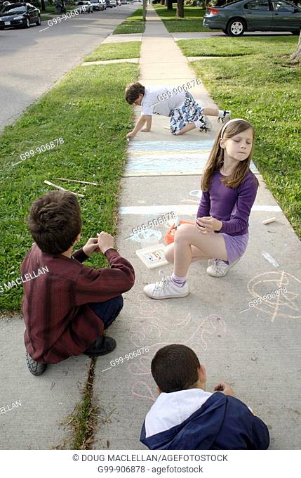 Canada, Ontario, Windsor. Three boys and one girl drawing with chalk on a sidewalk during the summer