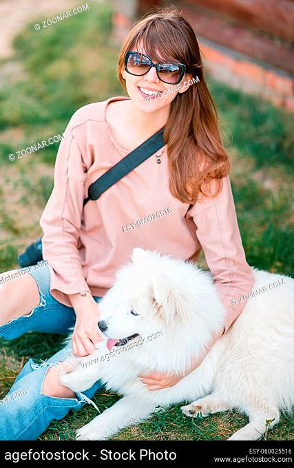 young stylish hipster woman girl playing white kid-skin dog in country side, village wood house, cool outfit, romantic mood, having fun, ripped jeans