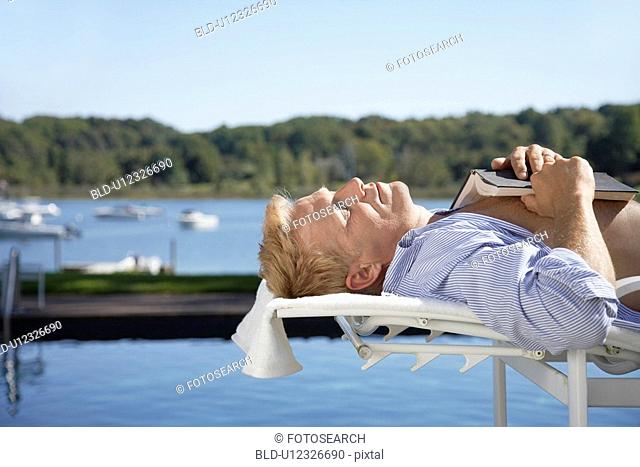 Man lying on lounge chair, book on chest
