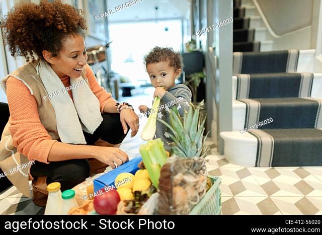 Mother watching cute baby girl eating celery from grocery delivery box