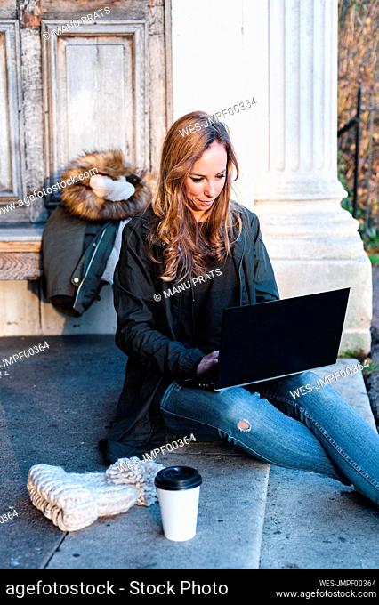 Beautiful businesswoman sitting on steps while laptop in park