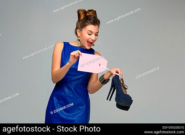 Beautiful happy woman holding pair of shoes. Price tag. Over grey background. Copy space