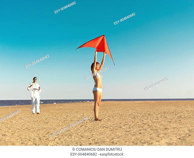 couple launching red kite on sea shore
