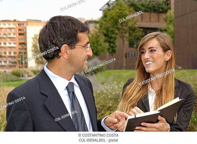 Two adults having discussion, looking at notebook