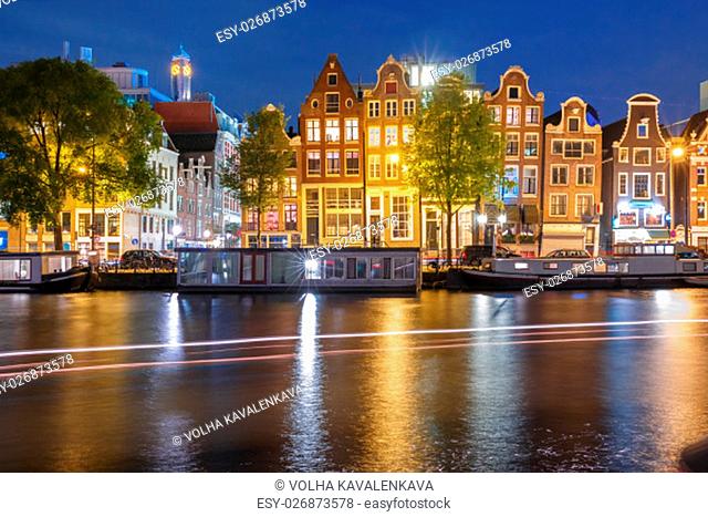 Amsterdam canal Amstel with typical dutch houses, houseboat and luminous track from the boat at night, Holland, Netherlands