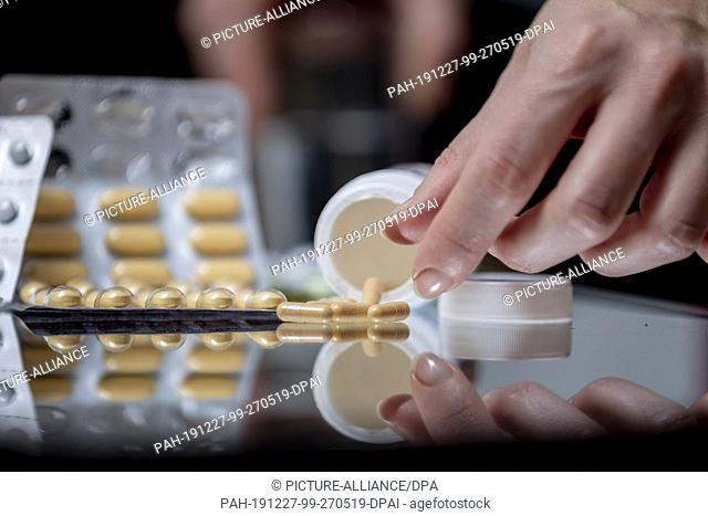 14 December 2019, Berlin: ILLUSTRATION - A woman reaches for tablets on a glass table. (posed scene, to dpa story: Painkiller - good thing and drug at the same...