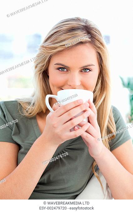 A close up shot of a woman looking forward, as she holds a mug up in front of her mouth