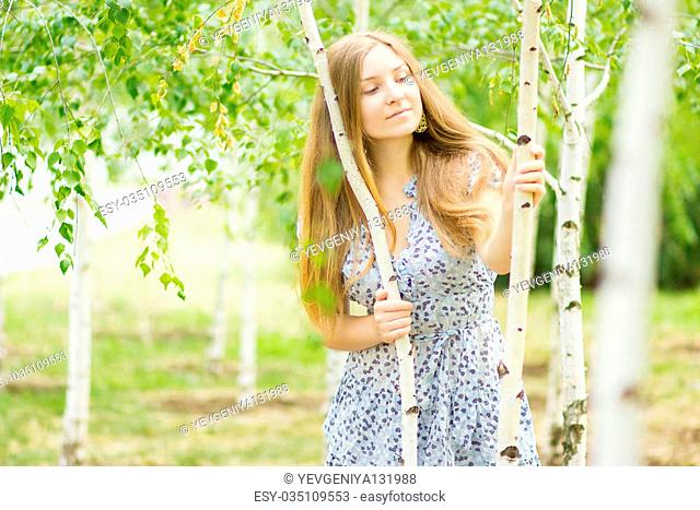 Portrait of a beautiful young woman with brown long hair on nature in a dress with a floral pattern. Girl resting in a birch forest