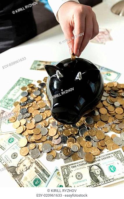 photo of hand putting coin in black piggy bank