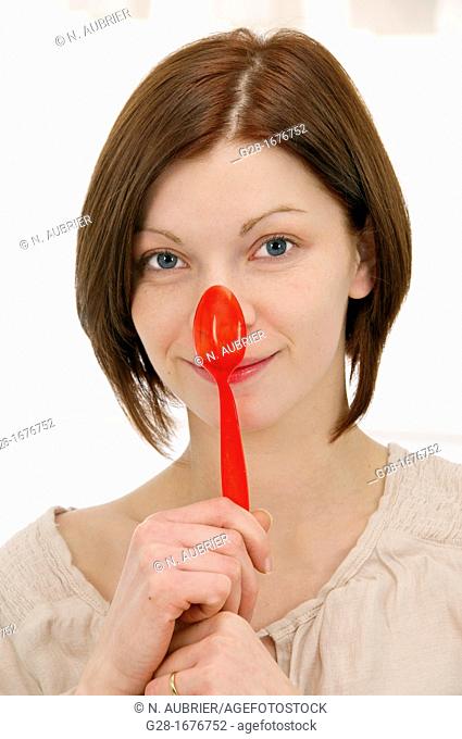 young smiling woman in beige, holding a red plastic teaspoon over her nose