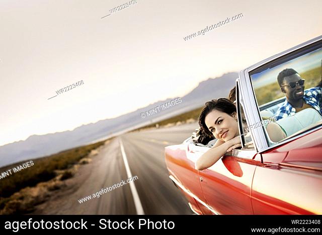 A group of friends in a red open top convertable classic car on a road trip