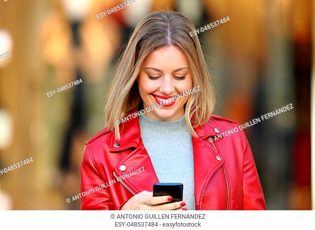 Front view portrait of a happy blonde using a smart phone in a mall