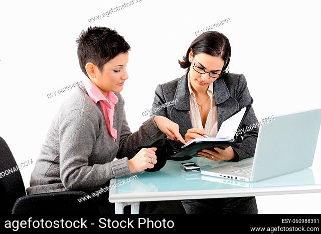 Young businesswomen sitting at office desk, working and talking. Isolated on white background