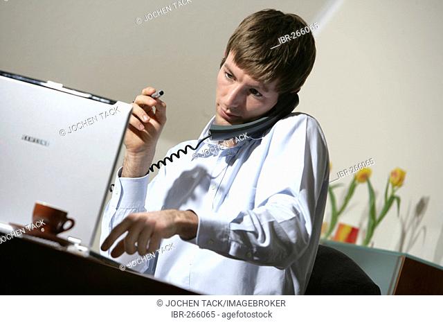 DEU, Germany : Young man is working at his laptop computer, on the phone