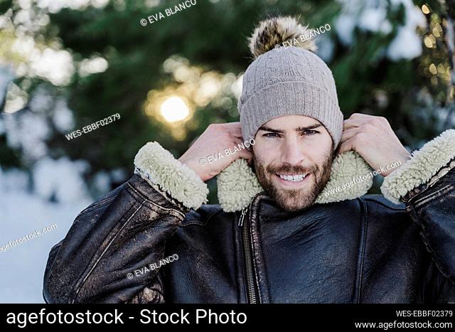 Smiling handsome man adjusting collar of jacket during winter