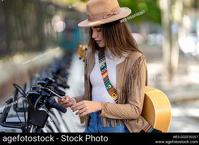 Young woman paying through smart phone at bicycle parking station