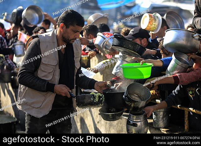 19 December 2023, Palestinian Territories, Rafah: Palestinians gather with pots to receive food at a donation point provided by a charitable organization in...