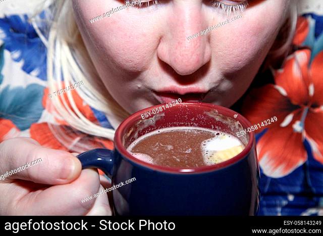 Woman drinking hot cocoa from a blue and red mug slowly