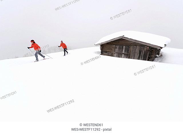 Italy, South Tyrol, Couple cross-country skiing, next to cabin