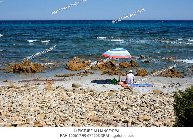 05 June 2019, Italy, Nuoro: A man has sat under a parasol on a beach in the National Park di Bidderosa in the Gulf of Orosei