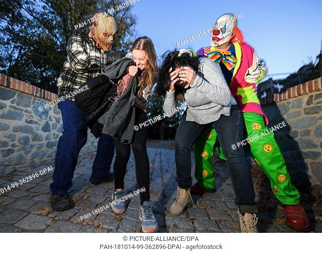 14 October 2018, Hessen, Muehltal: During the dress rehearsal, two visitors are followed by a horror clown and a scarred face