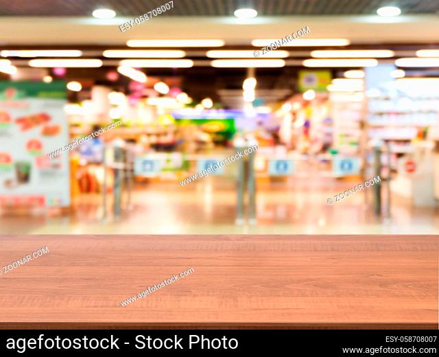 Wooden board empty table in front of blurred background. Perspective dark wood over blur in entrance area of supermarket
