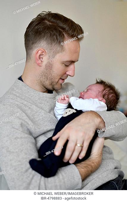 Young father keeps crying infant, 4 weeks, on arm, Baden-Württemberg, Germany