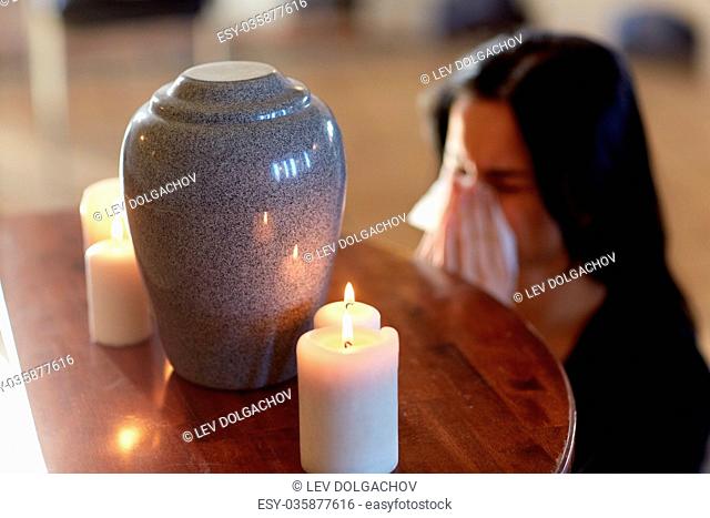 cremation, people and mourning concept - woman with wipe and cinerary urn crying at funeral in church