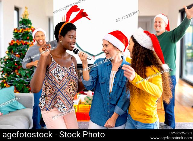 Image of happy diverse female friends singing karaoke celebrating christmas at home