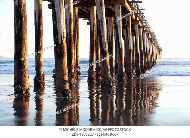 Cayucos pier pilings are reflected in the sandy water as the ocean waves come in