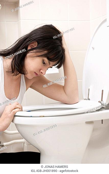 This picture shows a young caucasian woman with brown hair as she sits near her toilet feeling sick / ill in her bathroom