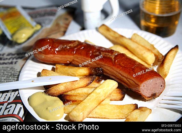 Sausage with mustard and chips on paper plate