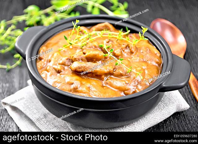 Beef goulash in tomato sauce with sprigs of thyme in a pan on a napkin, spoon, parsley on wooden board background