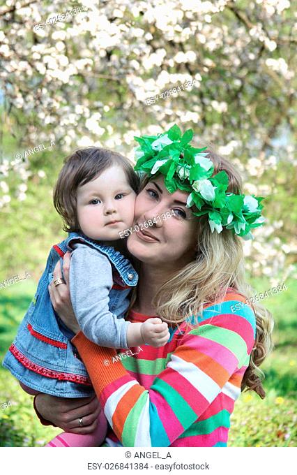 Mother in wreath hugging baby girl under spring tree