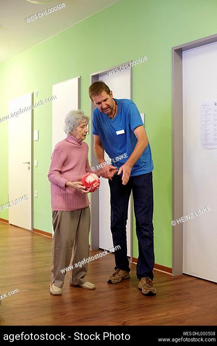 Geriatric nurse talking to age demented senior woman with foam ball in a nursing home